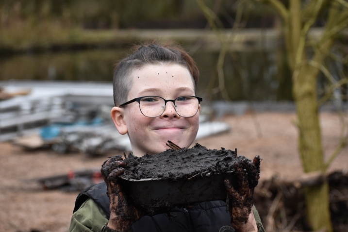 A child holds up his 'mud pie' that he has created in a mud kitchen